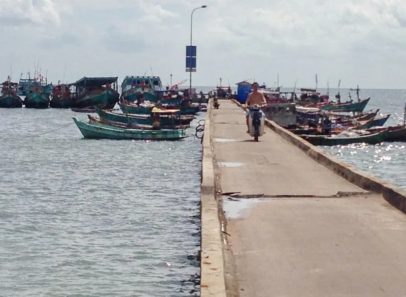 Một người đàn ông chạy xe máy trên cầu tàu bê tông có nhiều tàu cá đậu ở Hàm Ninh, Phú Quốc.